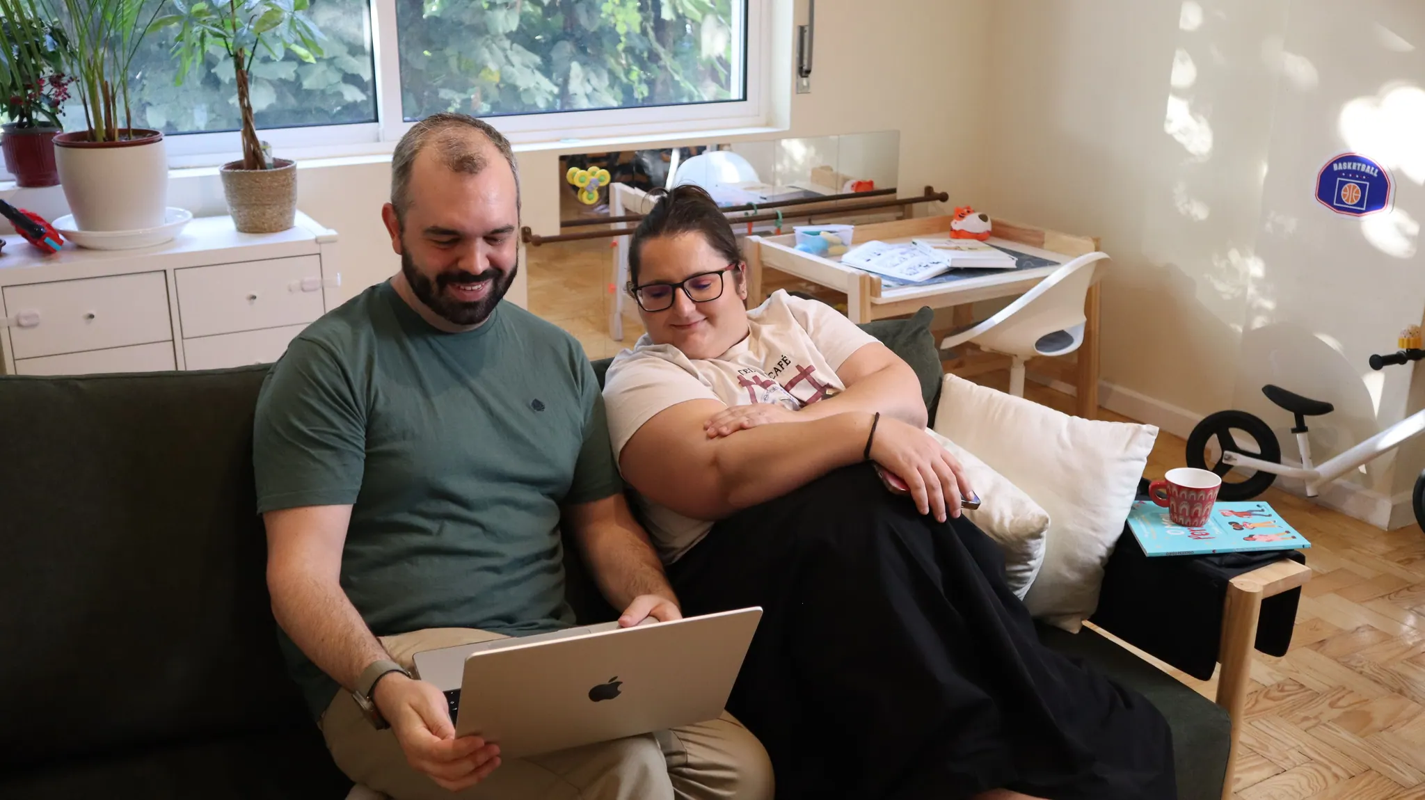 Rômulo e Verônica no sofá da sala, sorrindo para um notebook