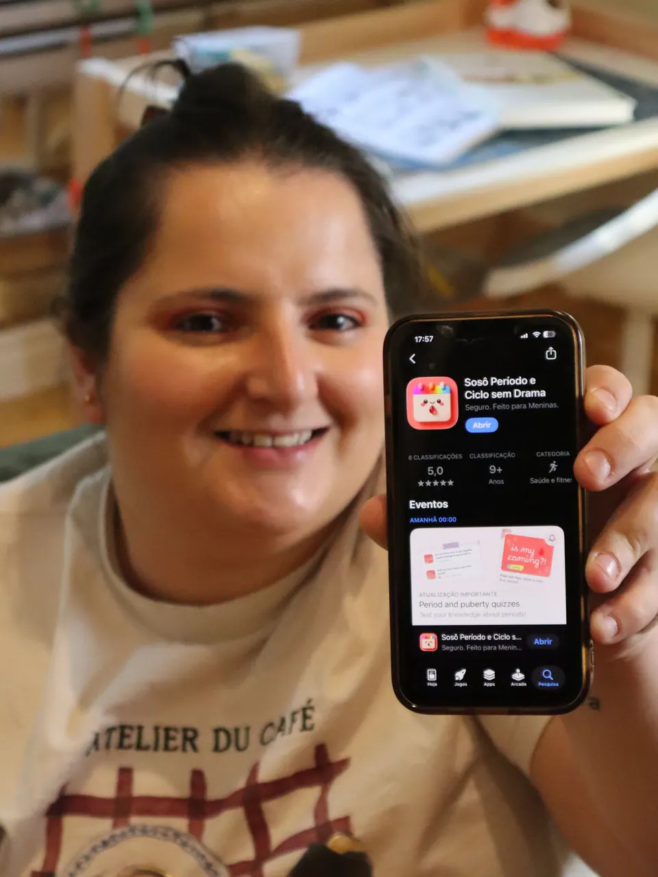 Verônica sorrindo e mostrando um celular com o app Sosô na App Store